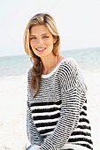 A young blonde woman on a beach wearing a black and white striped knitted jumper