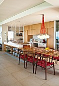 Island counter with extended table top and classic-style, dark wood chairs with red mesh seats in open-plan kitchen