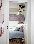 View into tiny bedroom with children's bunk beds anchored in walls in front of window and collection of soft toys under lowest bunk
