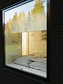 Swedish wooden house; trees reflected in bedroom window and view of bed