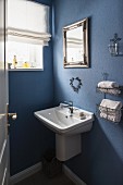 Waschbecken und Hängeregal mit Handtüchern an blau getönter Wand im Bad