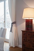 Selbstgebaute Tischleuchte mit Vintage Blechdose als Lampenfuss auf Kommode, daneben drapierter Vorhang an Terrassentür