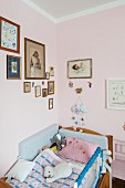 Soft toys on child's bed in corner below framed pictures on pink-painted walls