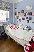 Einzelbett mit weiss lackiertem Holzgestell, gerahmte Bilder an fliederfarbener Wand in Kinderzimmerecke