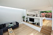 Offener, minimalistischer Wohnraum mit Sofa gegenüber Empore mit Brüstungsmauer vor Essbereich