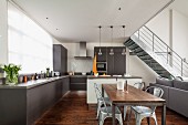 Open-plan interior in shades of grey with dining area and metal staircase in background