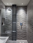 Designerbad - Duschbereich mit Glas Trennscheibe, an Wand raumhohes Metall Regal vor gefliester Wand mit dreidimensionaler Oberfläche