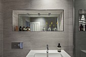 Washbasin on tiled wall below mirror in niche