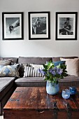 Retro Schwarzweissfotos über Sofa mit Kissensammlung; Blumenstrauss und Teelichter in Blautönen auf Truhentisch