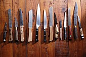 A row of different knives on a wooden surface
