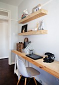 Untreated wooden shelves above wooden desk in home office with vintage telephone and classic chair