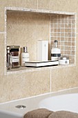 Sand-coloured tiles on wall and in niche with toiletries above bathtub