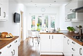 Open-plan fitted kitchen with white fronts and wooden work surfaces; dining area with French windows leading to garden
