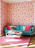 Weisser Retro Couchtisch vor türkisblauem Sofa in Wohnzimmerecke mit Blumentapete