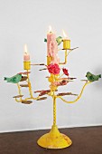 Brennende Kerzen auf gelb lackiertem, romantischem Kerzenhalter mit Vogelfiguren und Blumenmotiven dekoriert