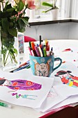 Colourful drawings of geisha and mug of pens on table