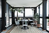 Seating area with delicate, white metal chairs and arc lamp in black conservatory of penthouse apartment