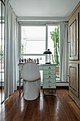 White, classic shell chair at desk in narrow room with floor-length curtains on windows