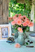 Salmon pink dahlias in green ceramic jug next to hydrangea in blue china teacup and picture hand-crafted from old postcard