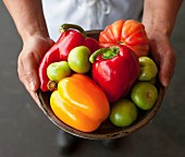 A chef holding a bowl of peppers, tomatillos and tomatoes