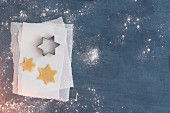 Unbaked star-shaped biscuits and a star-shaped cutter on a piece of parchment paper