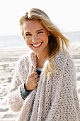 Junge, blonde Frau in beigefarbener Strickjacke am Meer