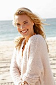 A young blonde woman by the sea wearing a white woollen jumper