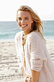 A young blonde woman by the sea wearing a white woollen jumper