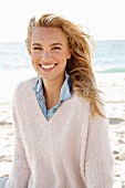 A young blonde woman by the sea wearing a denim shirt and a white woollen jumper