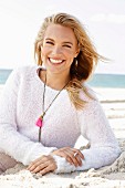 A young blonde woman by the sea wearing a light knitted jumper