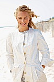 A young blonde woman on a beach wearing a white coat