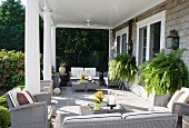 Überdachte Terrasse mit Säulenkolonnade und eleganten, grauen Rattanmöbeln; üppige Farnpflanzen an Hausfassade