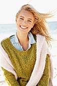 A young blonde woman by the sea wearing a knitted jumper and a denim shirt