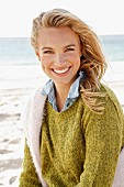 Junge, blonde Frau mit Strickpullovern und Jeanshemd am Meer