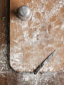 Flour and a knife on a chopping board (seen from above)