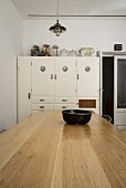 Vintage-Küchenschrank an weisser Wand; im Vordergrund ein heller, massiver Holztisch
