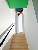 Pale wooden staircase with black handrail in narrow stairwell with copper-coloured pendant lamps over landing and green-painted ceiling