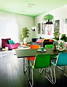 Colourful plastic chairs at black table below spherical pendant lamp; lounge area with sofa and beanbag below green-painted ceiling in modern interior