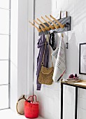A homemade coat rack made from wooden hangers mounted onto a wooden board next to a narrow wall table against a whitewashed brick wall