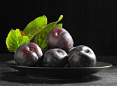 Black plums with leaves on a black plate