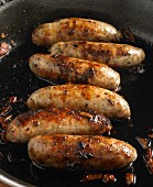 Six sausages frying in a pan