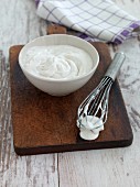 Whipped vegan egg whites in a bowl and on a whisk