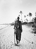 Black and white photo of African man wearing traditional clothing and sandals on beach
