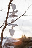 Garland of white-painted twigs, balls and hearts hanging from leafless branch