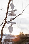 Weiß getünchte Holzstückchen, Kugeln und Herzen als Girlande an kahlen Zweigen