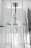 A glazed shower cubicle with a double swing door, a rain shower head and the hand-held shower head on a white tiled wall