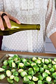 Köchin gießt Olivenöl auf Rosenkohl