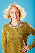 A young blonde woman with a hand on her hip wearing an olive green knitted jumper