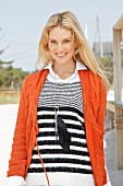 A young blonde woman outside wearing a black-and-white stripped jumper and an orange knitted cardigan