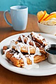 French toast with icing sugar and cream served with syrup, oranges, bananas and coffee